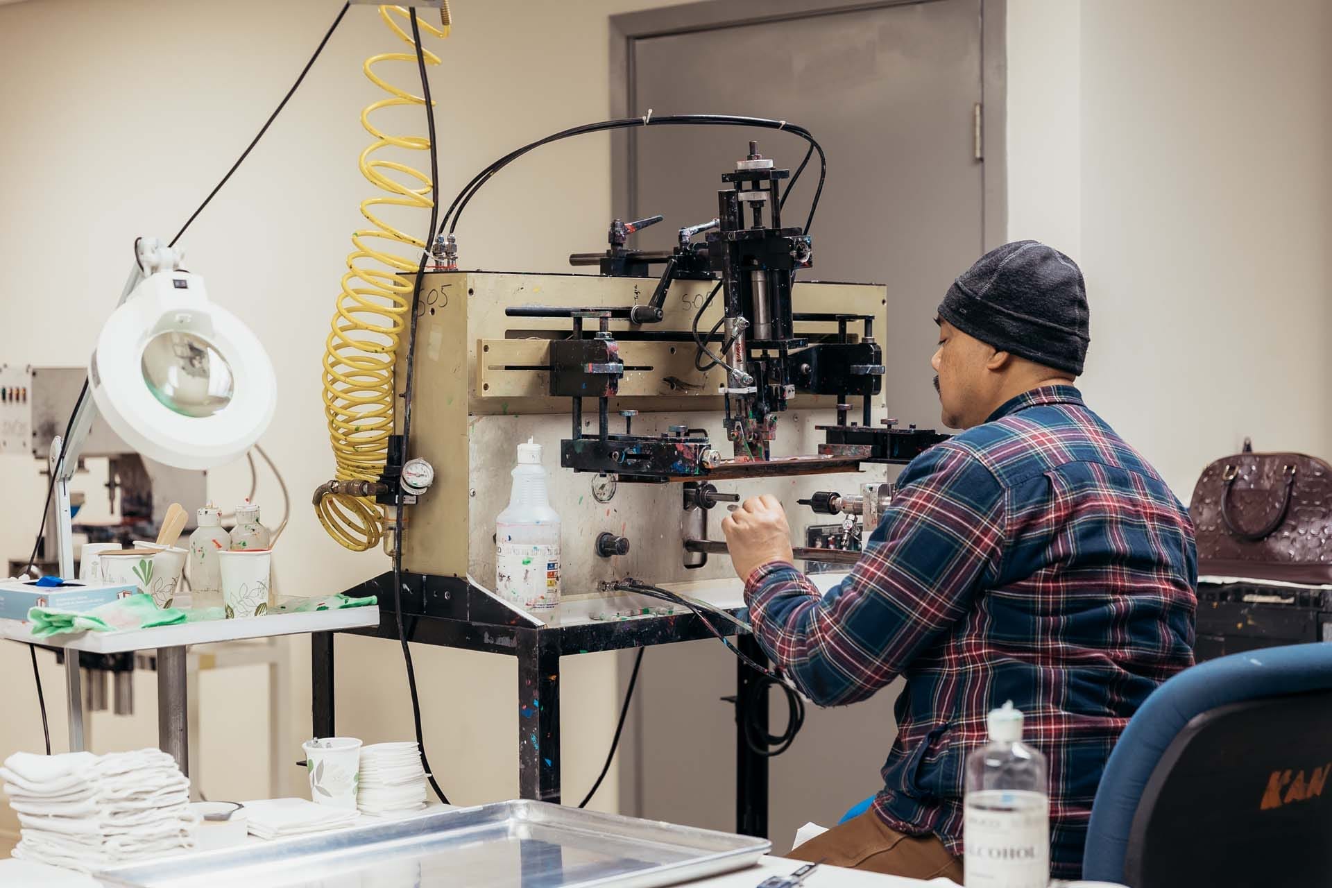 Technician operating a pad printing machine in a workshop, adjusting components during a small-scale manufacturing process.